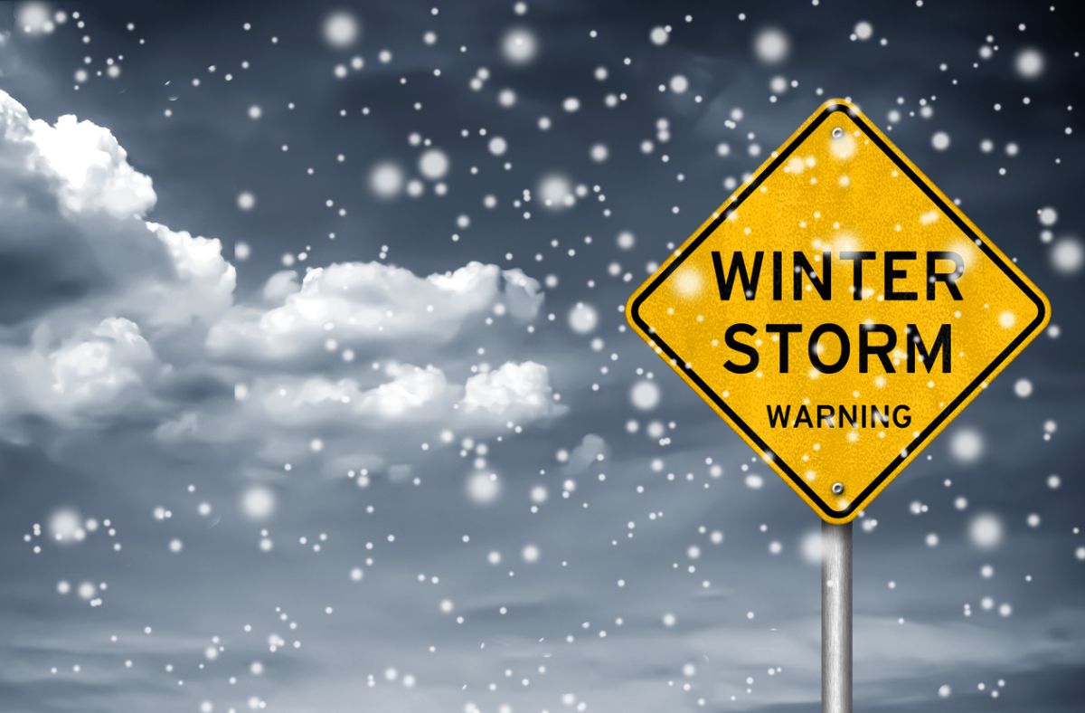 Winter storm warning road sign with falling snow and dark clouds, symbolizing extreme weather conditions driving increased energy demand and natural gas market volatility.